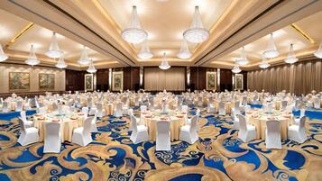 A large banquet hall with round tables, white chairs, and chandeliers.