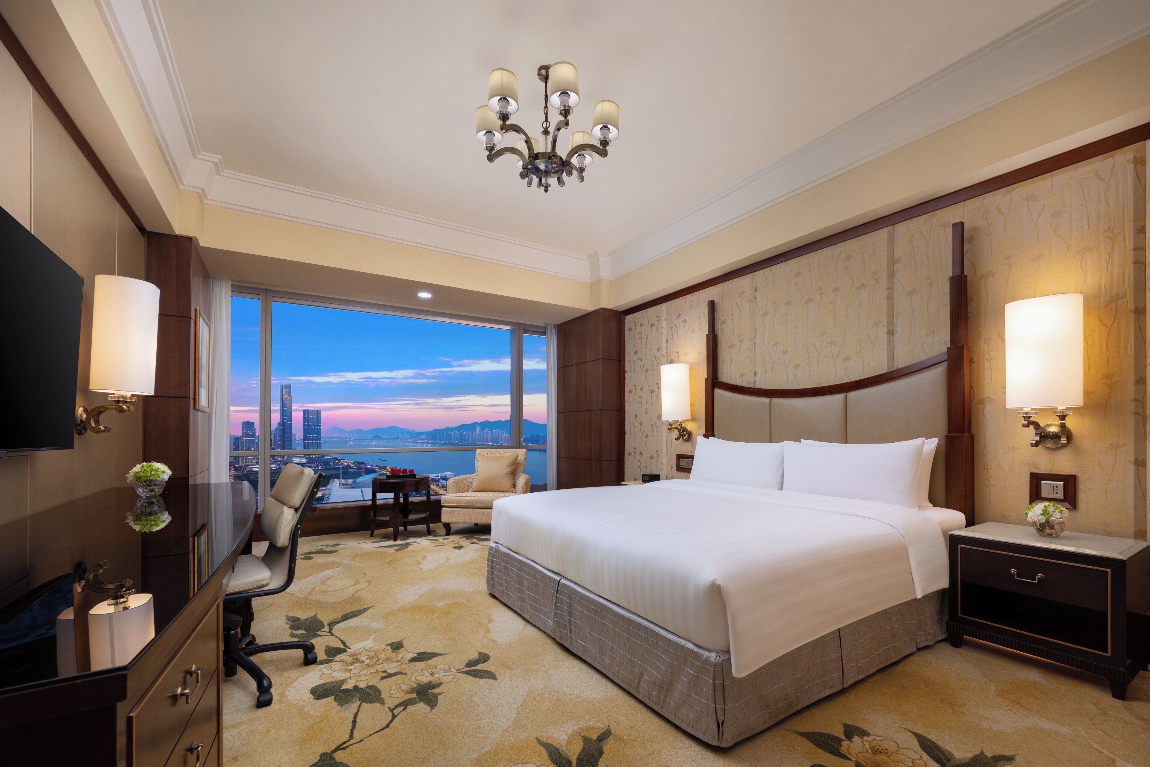 Habitación de hotel con una cama grande, un escritorio con silla, televisor y vistas a la ciudad.