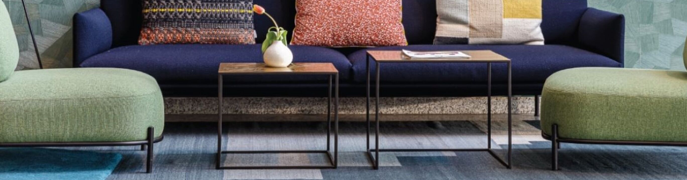 A modern living room with a dark blue sofa, two green armchairs, and two small wooden tables.