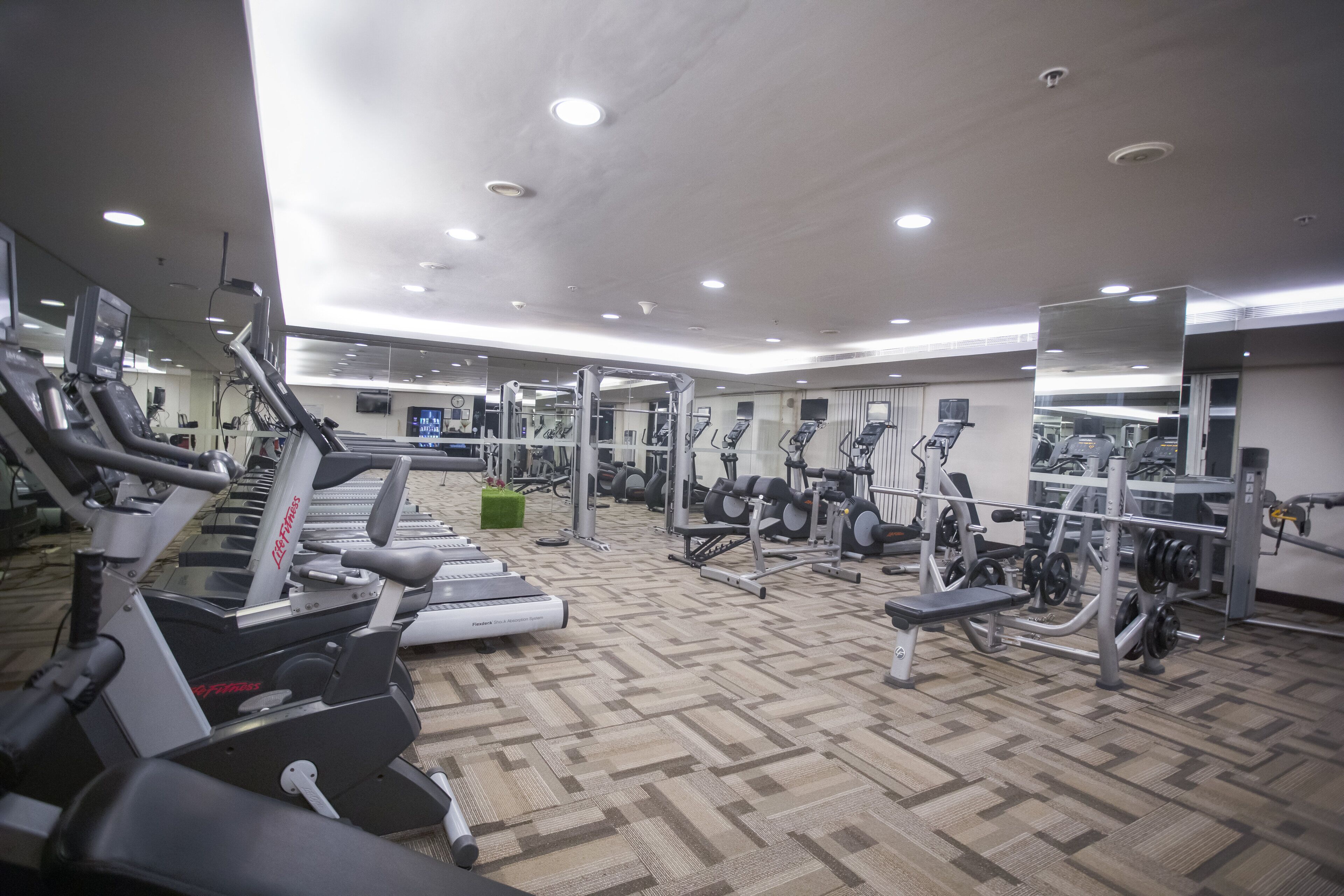 Un gimnasio con cintas de correr, máquinas de pesas y espejos.