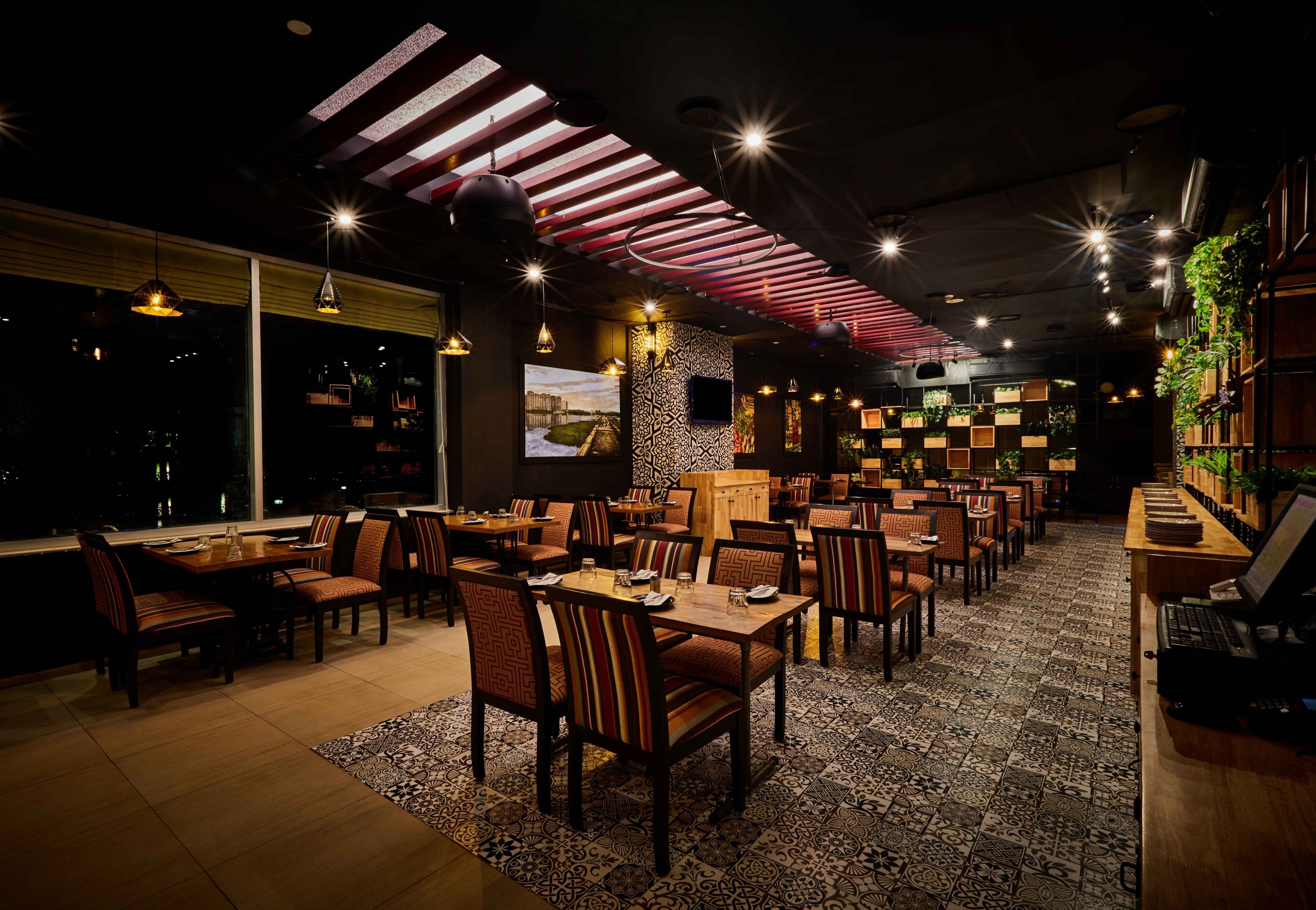 Un restaurant doté de nombreuses tables et chaises, d’un tapis à motifs et d’un plafond avec des lambris rouges.