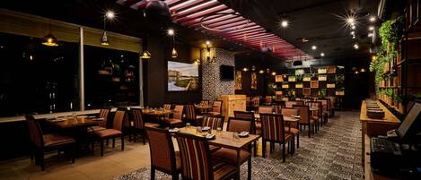 Un restaurant doté de nombreuses tables et chaises, d’un tapis à motifs et d’un plafond avec des lambris rouges.