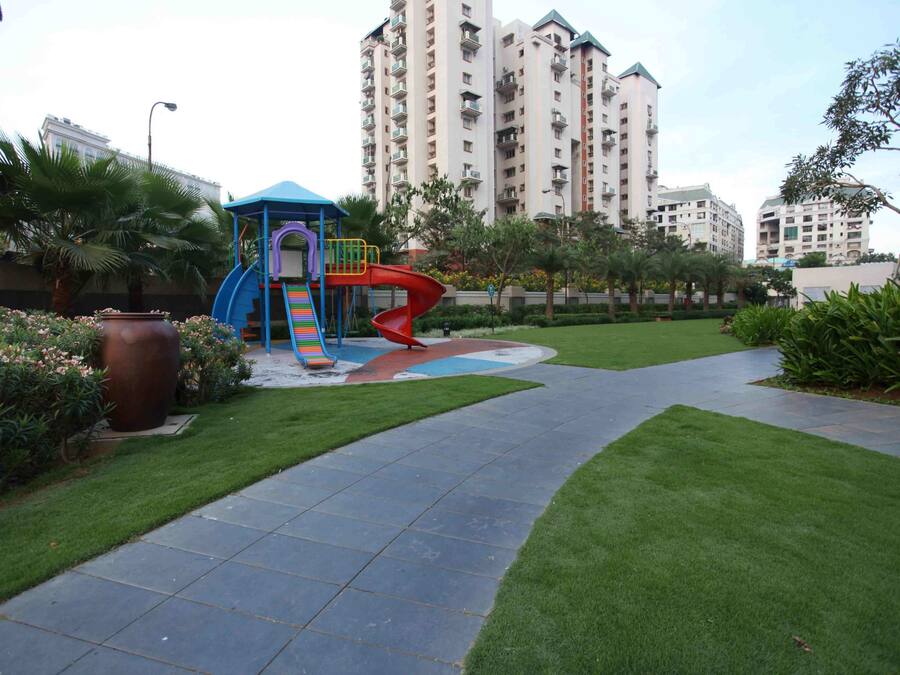 A playground with a slide and a climbing structure, surrounded by well-maintained grass and a paved walkway.