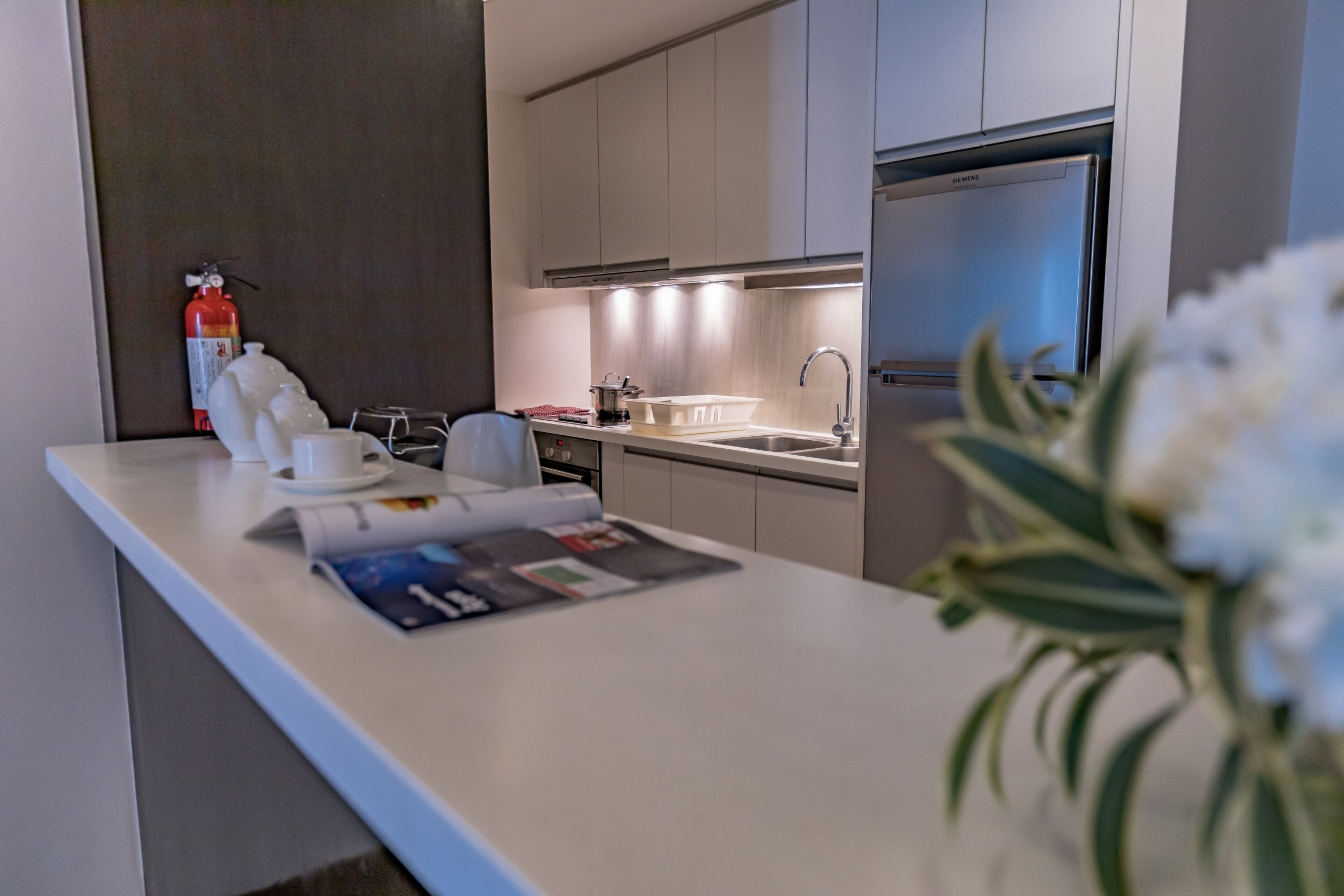 A modern kitchen with a built-in oven, a sink, and a stainless steel refrigerator.