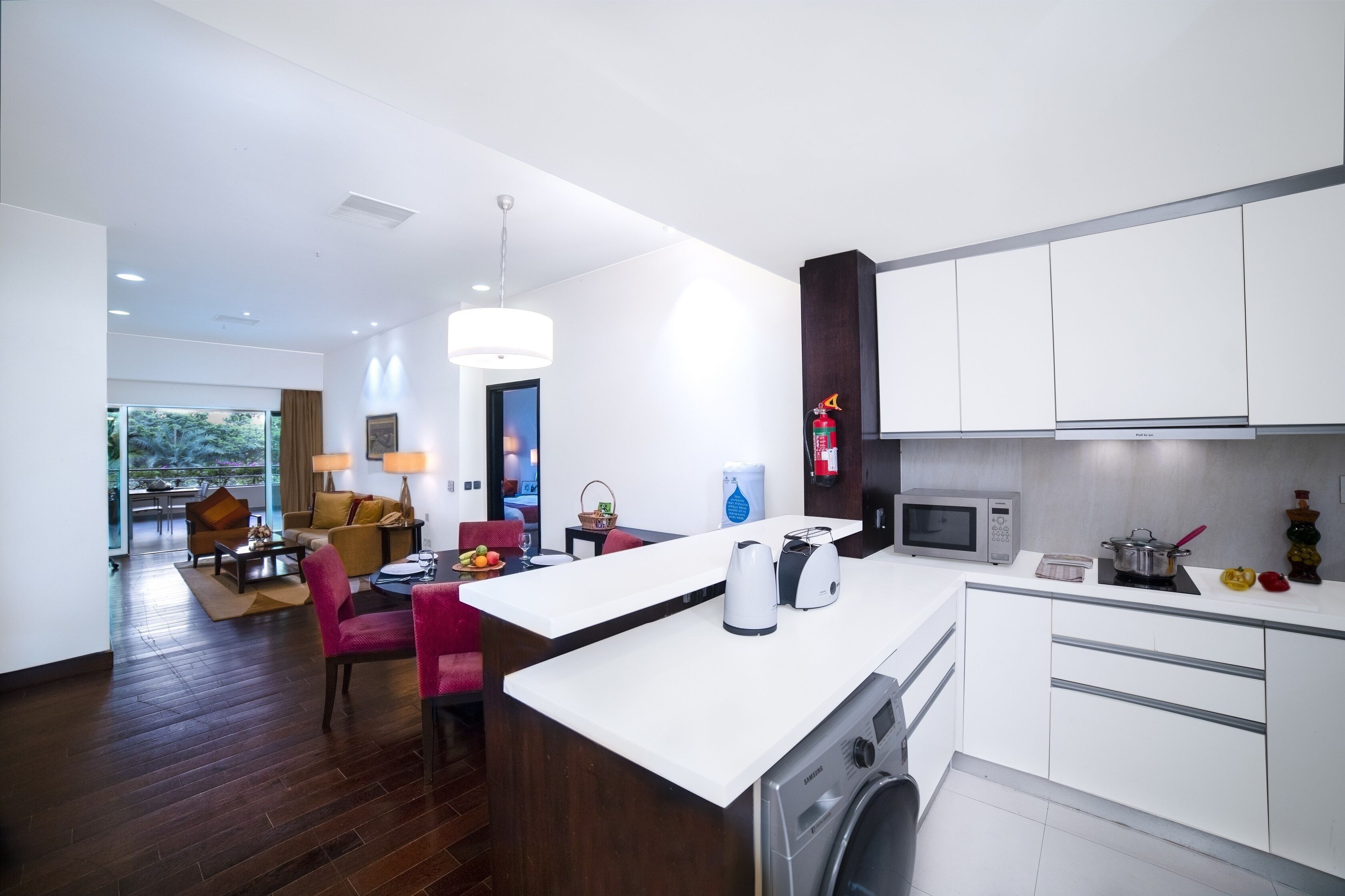 Una cocina moderna con lavadora y secadora integradas, un comedor con una silla roja y una sala de estar con sofá y mesa de centro.