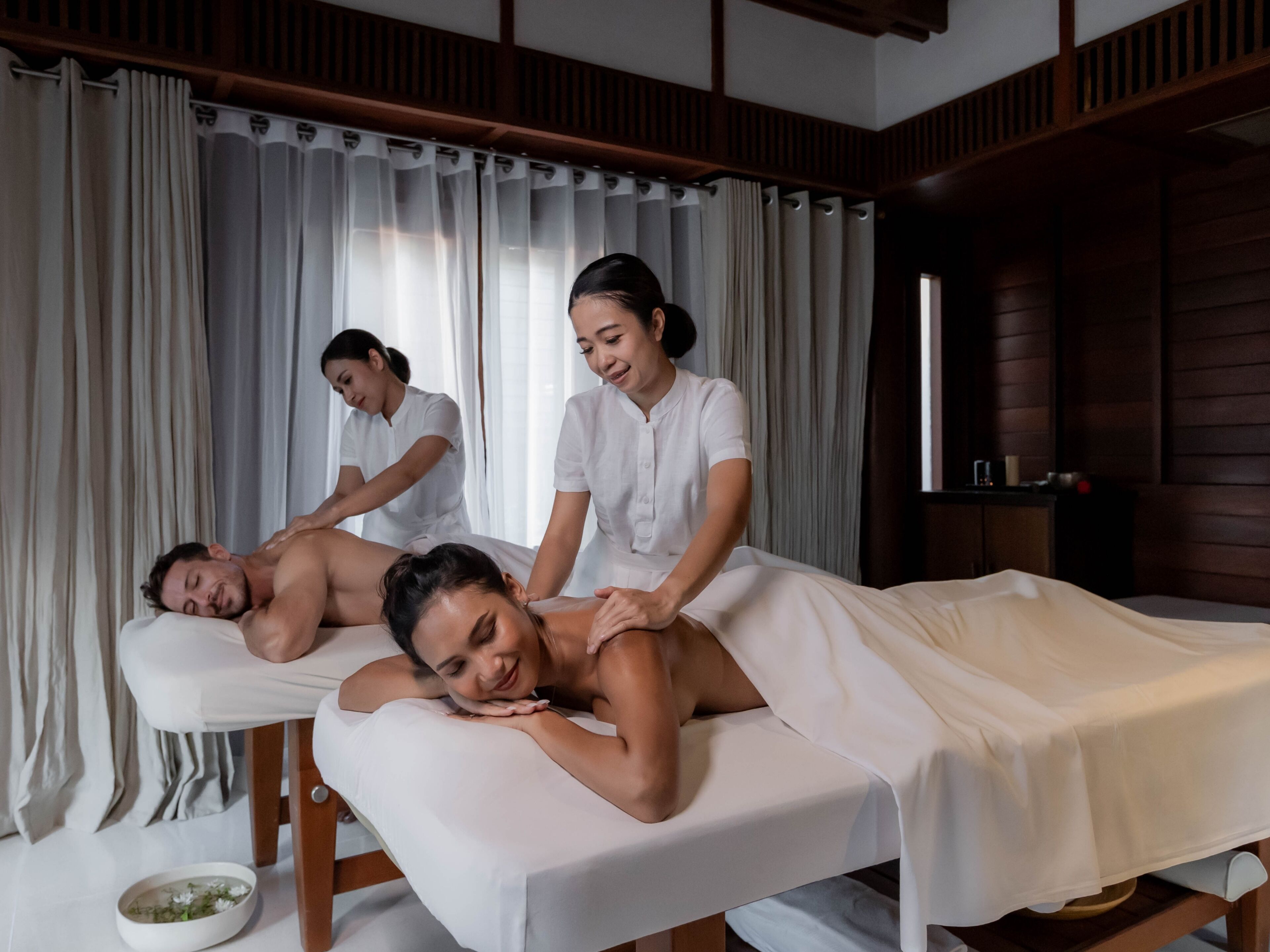 A massage therapy room with a wooden interior, a massage table, and a bowl of flowers on the floor.
