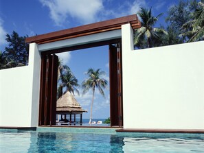 Piscina infinita com estrutura de colmo e palmeiras ao fundo.