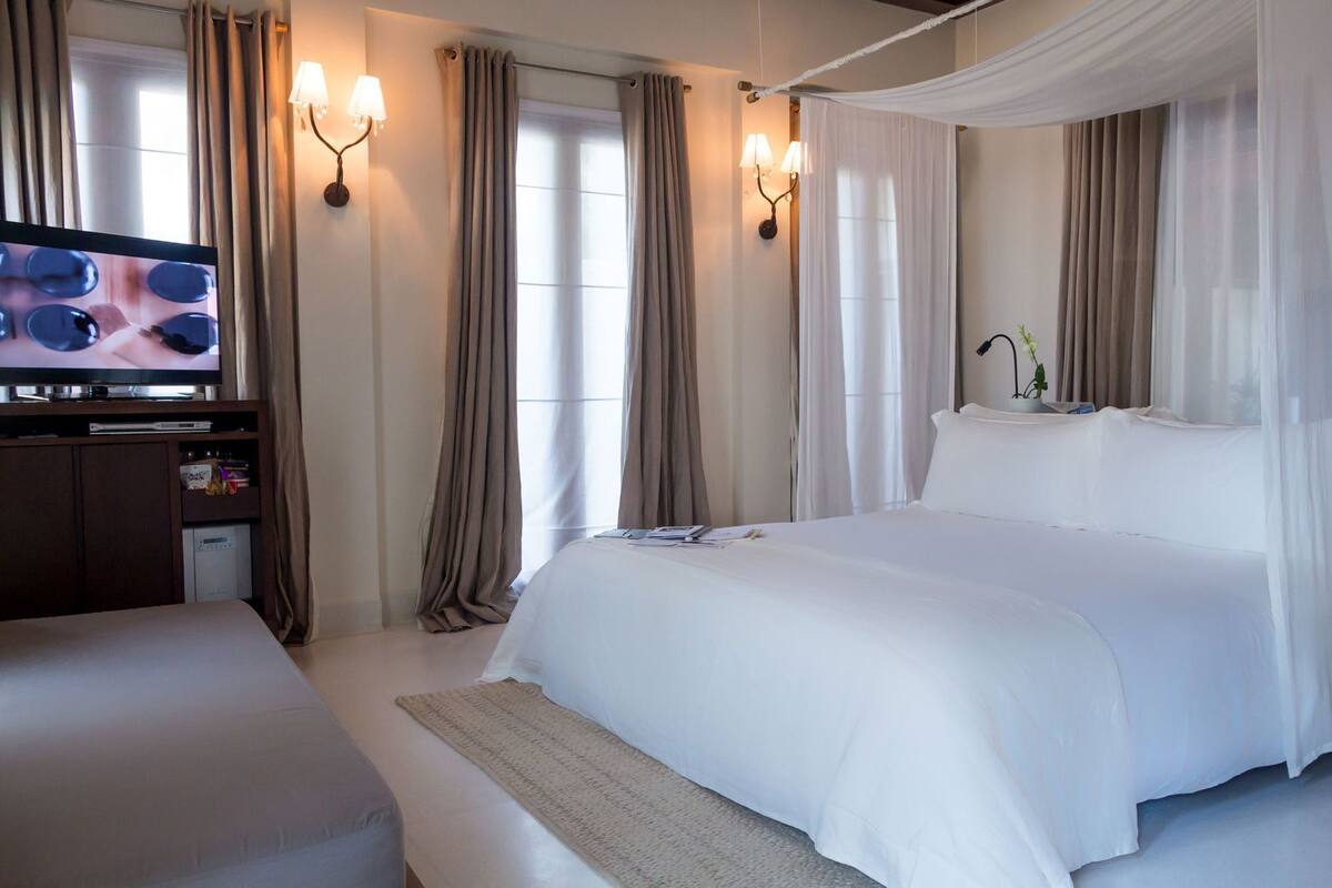 A hotel room with a large bed, a TV, a desk, and curtains.