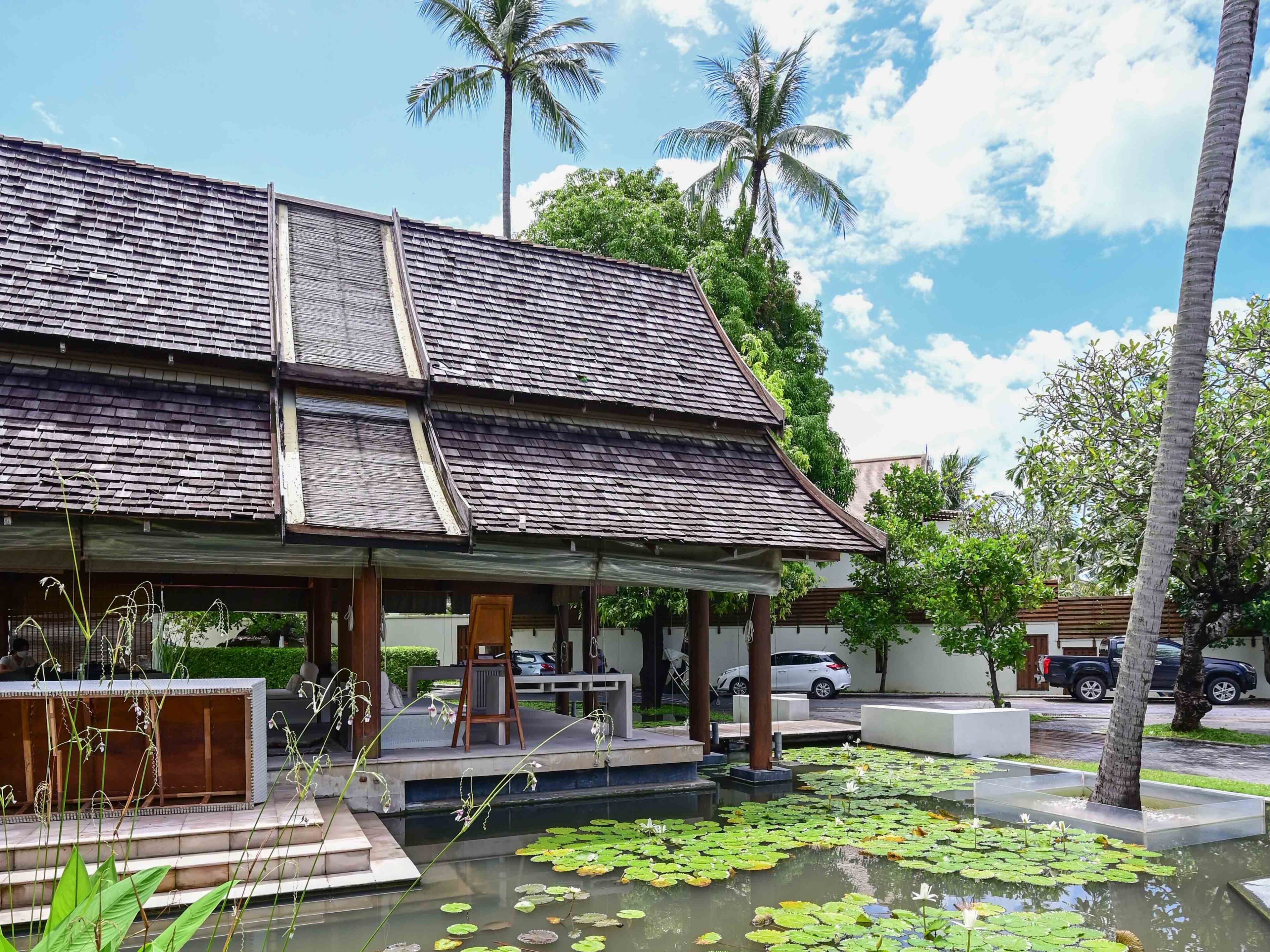 A traditional building with a tiled roof and a covered outdoor area with steps leading to a pond with lily pads.