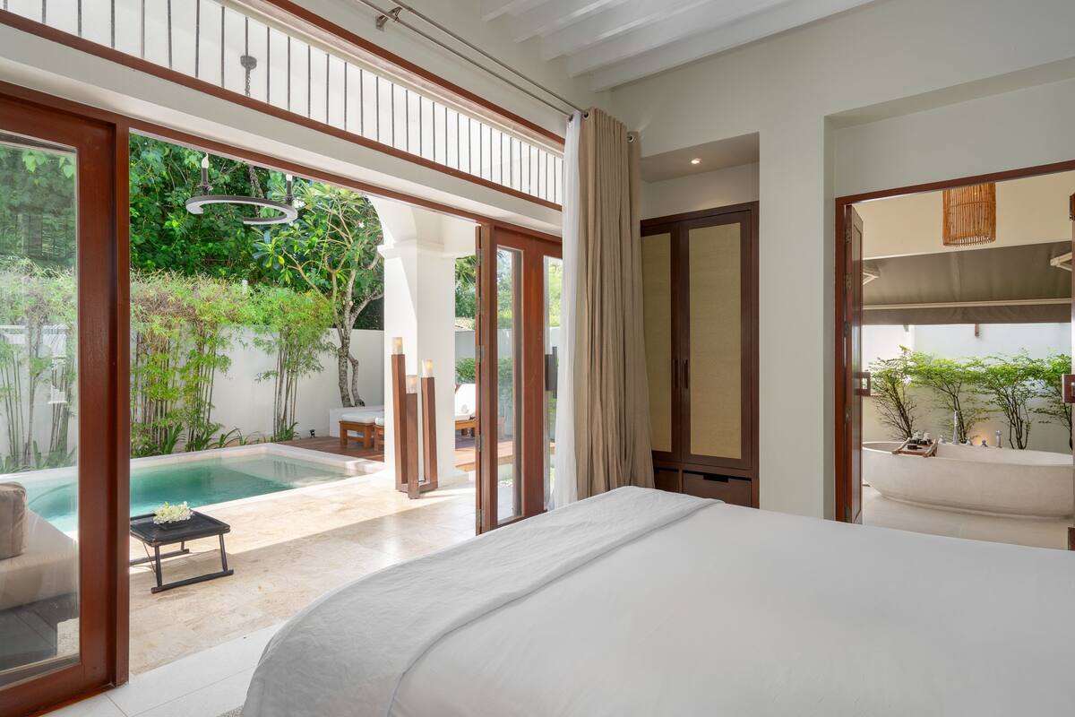 A bedroom with a large bed, a view of a swimming pool, and a bathroom with a bathtub.