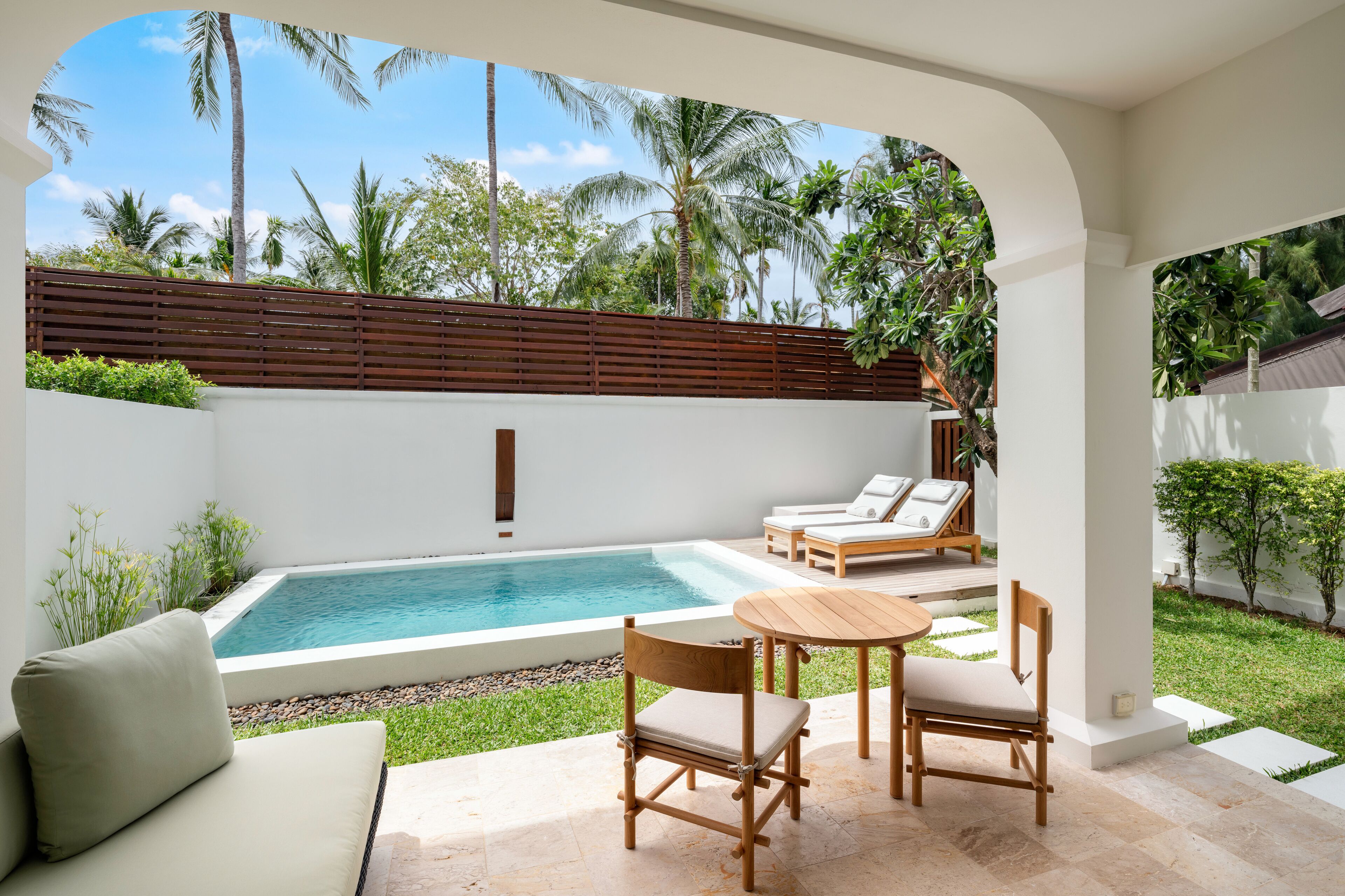 Un espace aménagé au bord de la piscine, avec une table et des chaises en bois, un canapé et des fauteuils de relaxation.