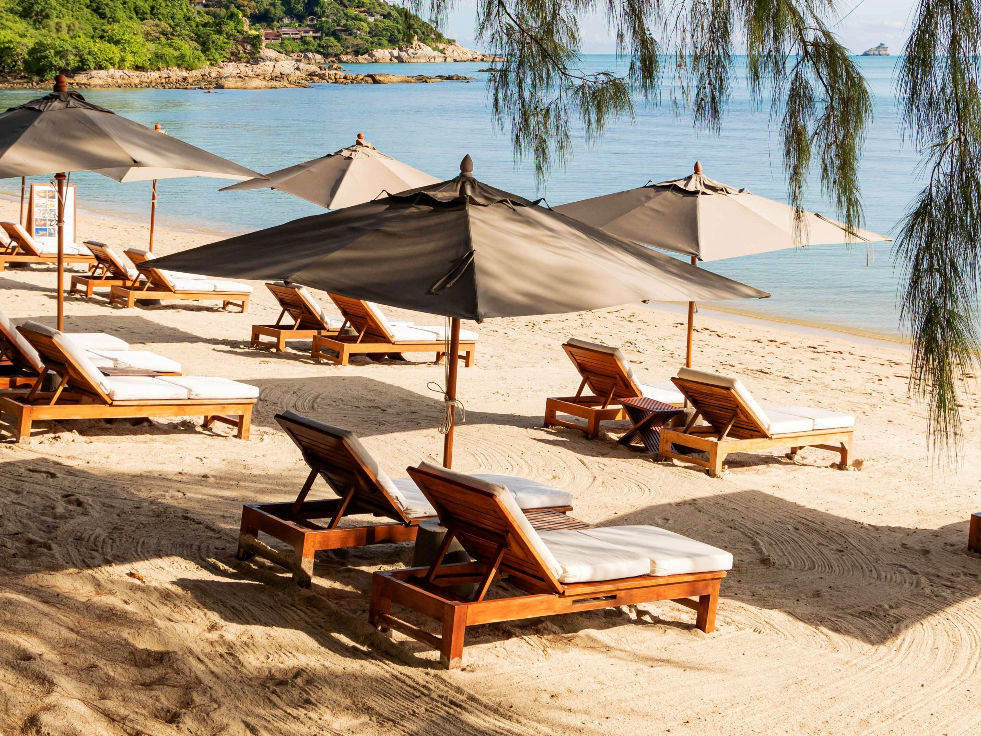 Ein Strand mit Holzliegen und großen Sonnenschirmen.
