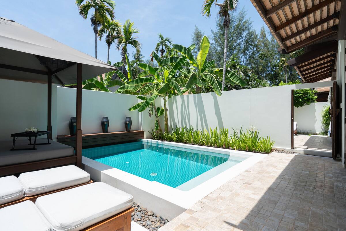 A modern outdoor pool area with a tiled deck, lounge chairs, and a covered seating area.