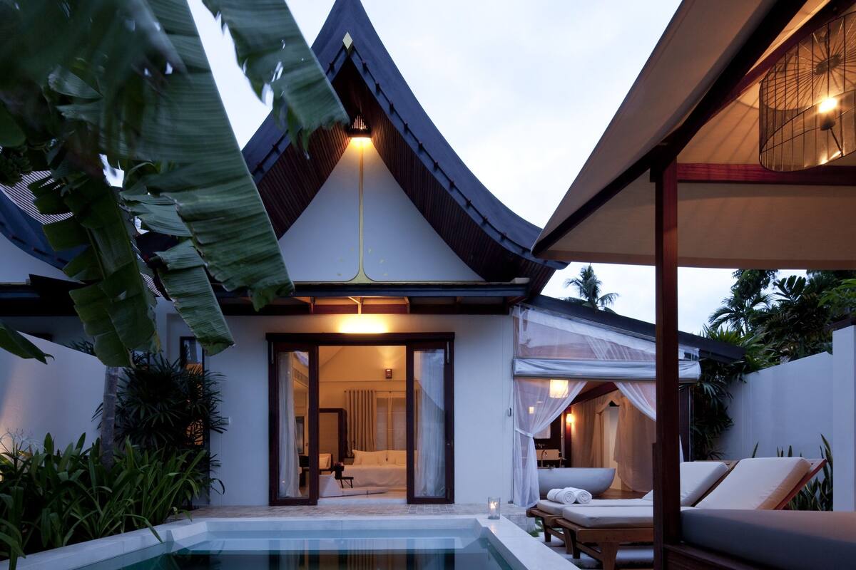 A modern pool area with a clear view of the pool, lounge chairs, and a building with a sloped roof.