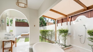 A modern bathroom with a freestanding bathtub, a shower area, and a small seating area with a view of the garden. - SALA Samui Choengmon Beach (Koh Samui)