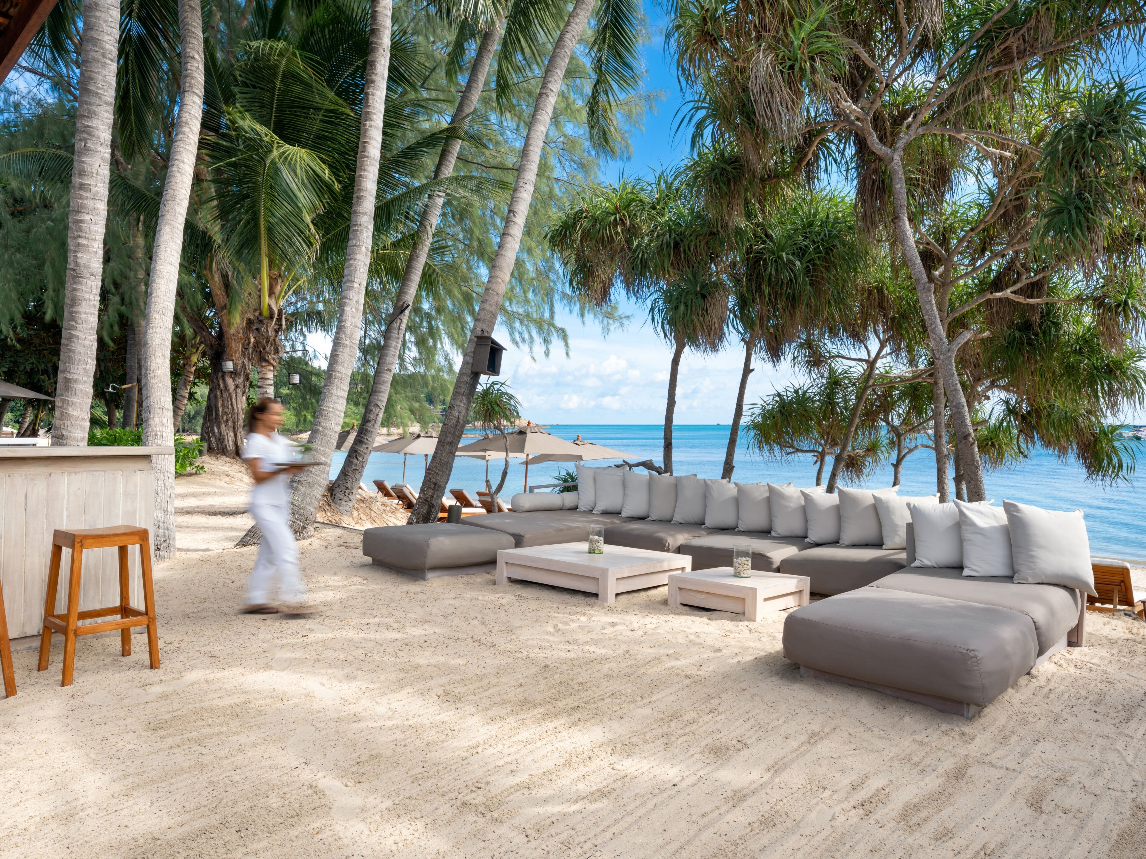 Eine Strandlounge mit einer Couch, Sesseln und einer Bar.