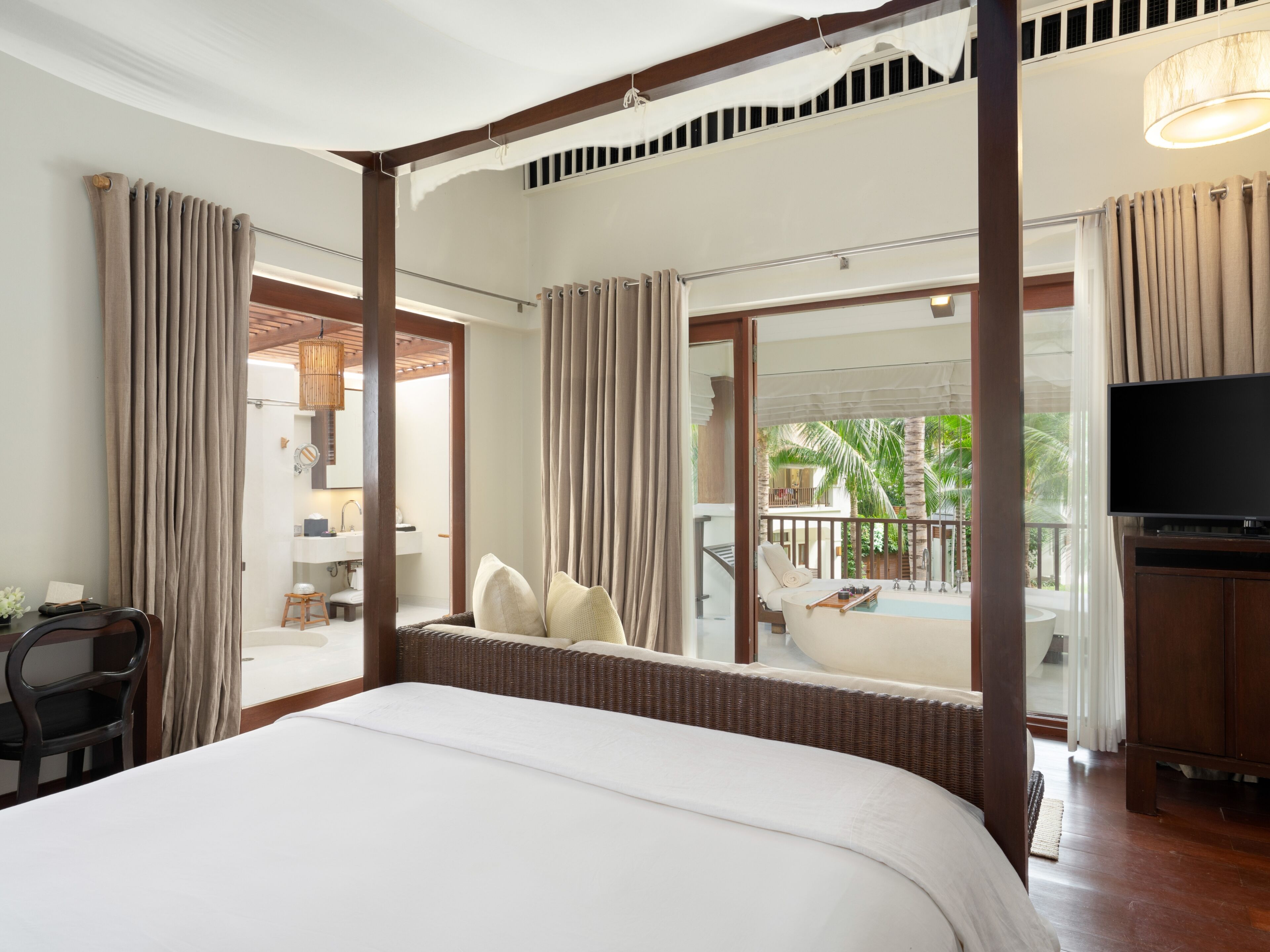 Une chambre d’hôtel avec un grand lit, une télévision et un balcon donnant sur des palmiers.