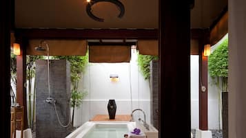 Un espace détente avec un jacuzzi, une douche et un tabouret en bois sur lequel sont posées des serviettes.