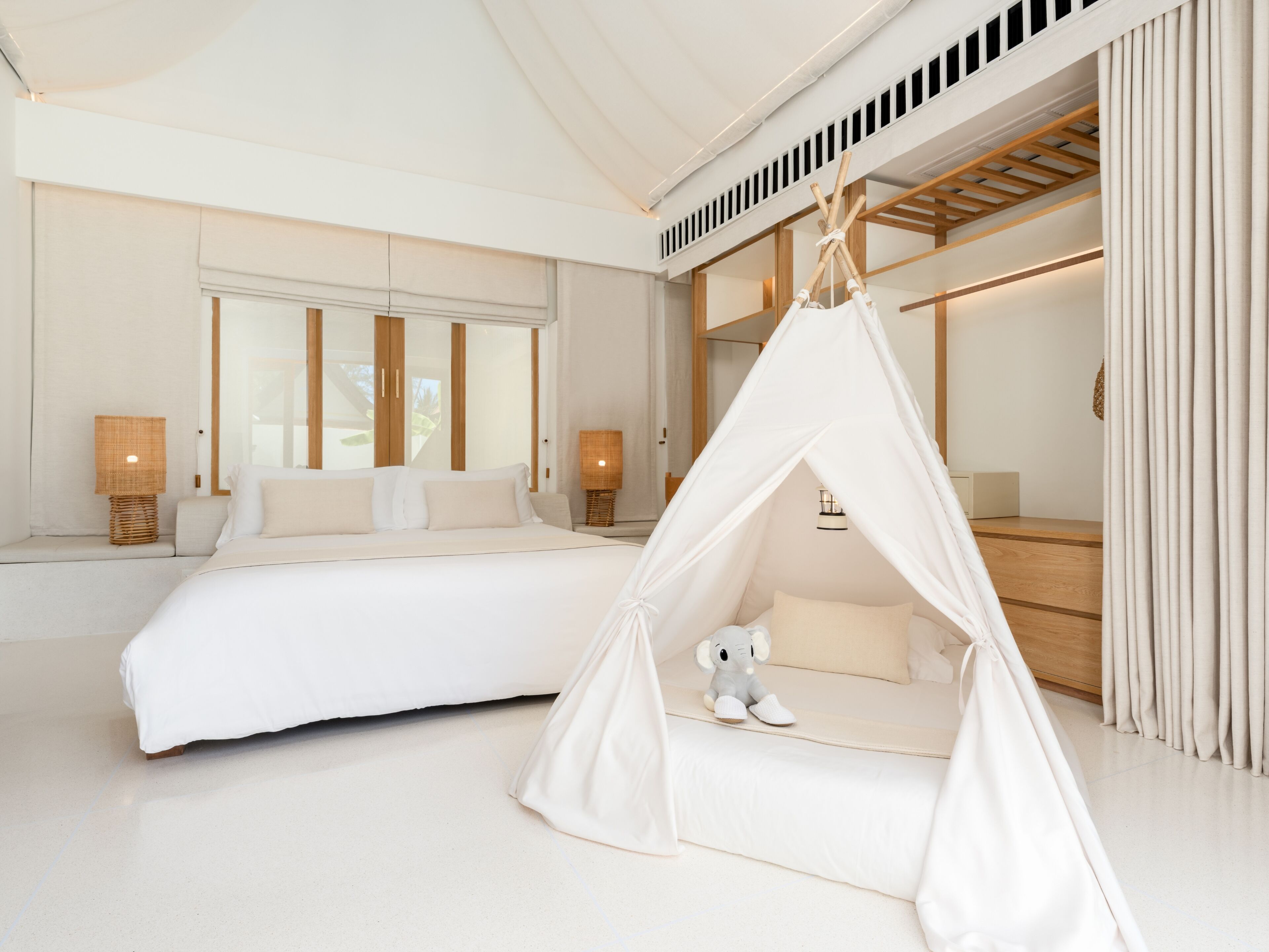 A modern bedroom with a large bed, a canopy bed, and a small seating area with a toy elephant.