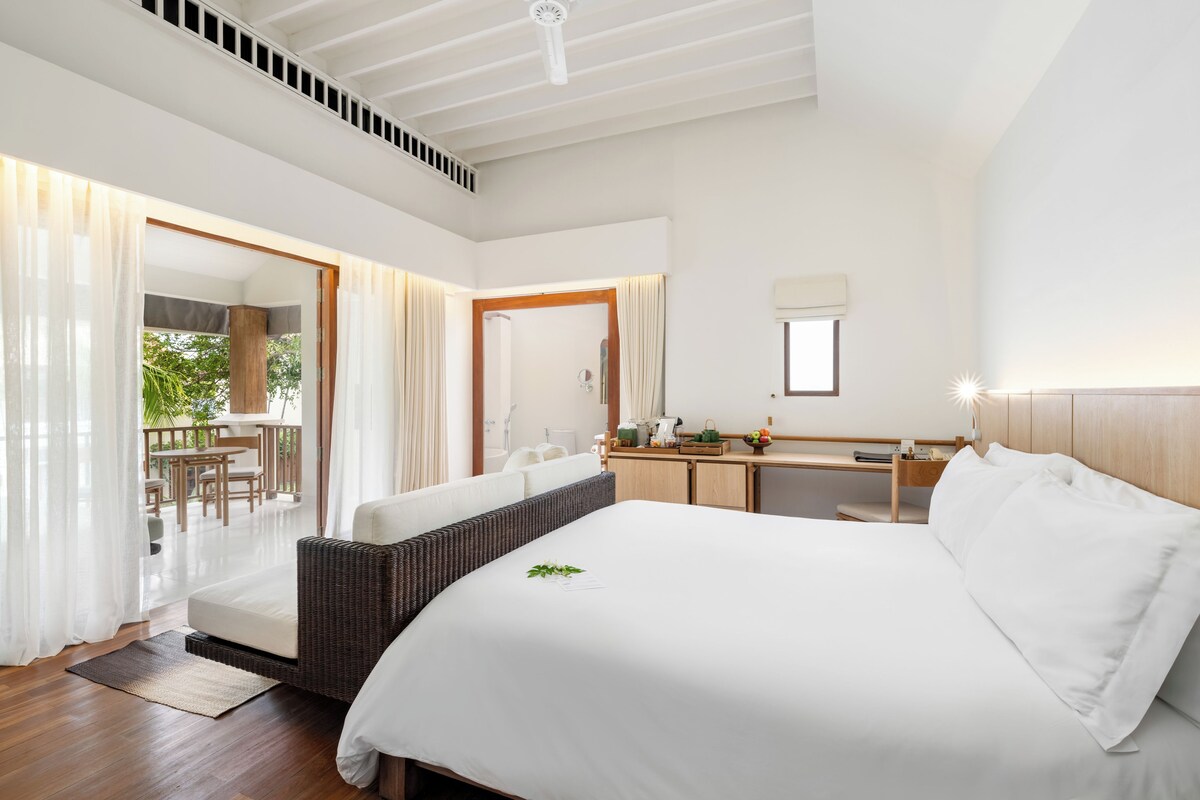 A spacious bedroom with a large bed, a wooden headboard, a bedside table, and a view of an outdoor patio area.