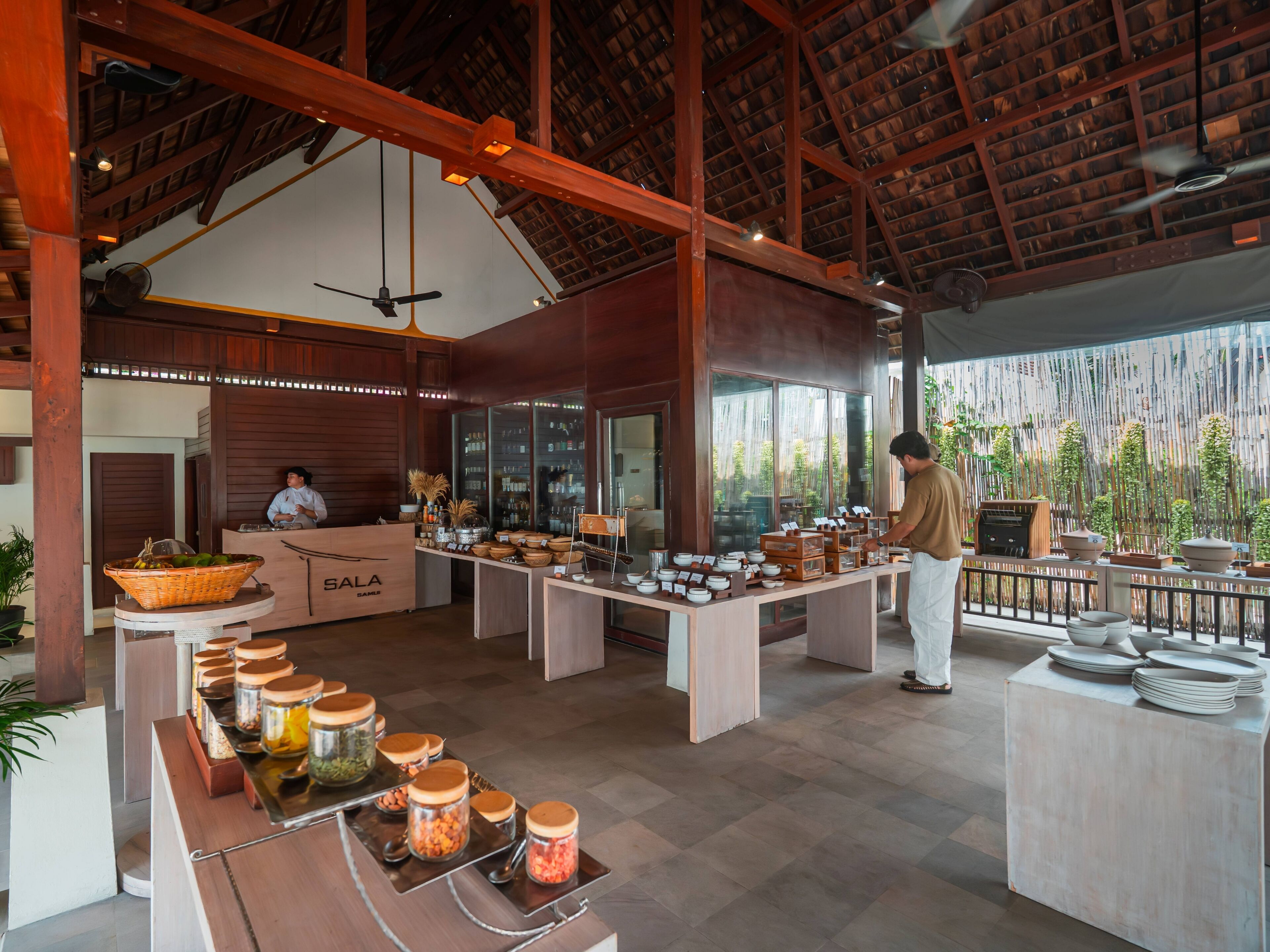 Um restaurante espaçoso com teto alto e vigas de madeira, apresentando um buffet com diversos alimentos e acompanhamentos.