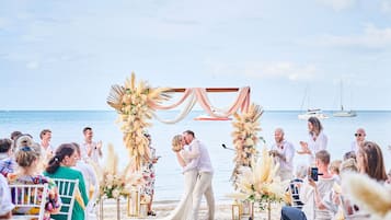 Cerimônia de casamento na praia, com um casal se beijando sob um arco de flores.