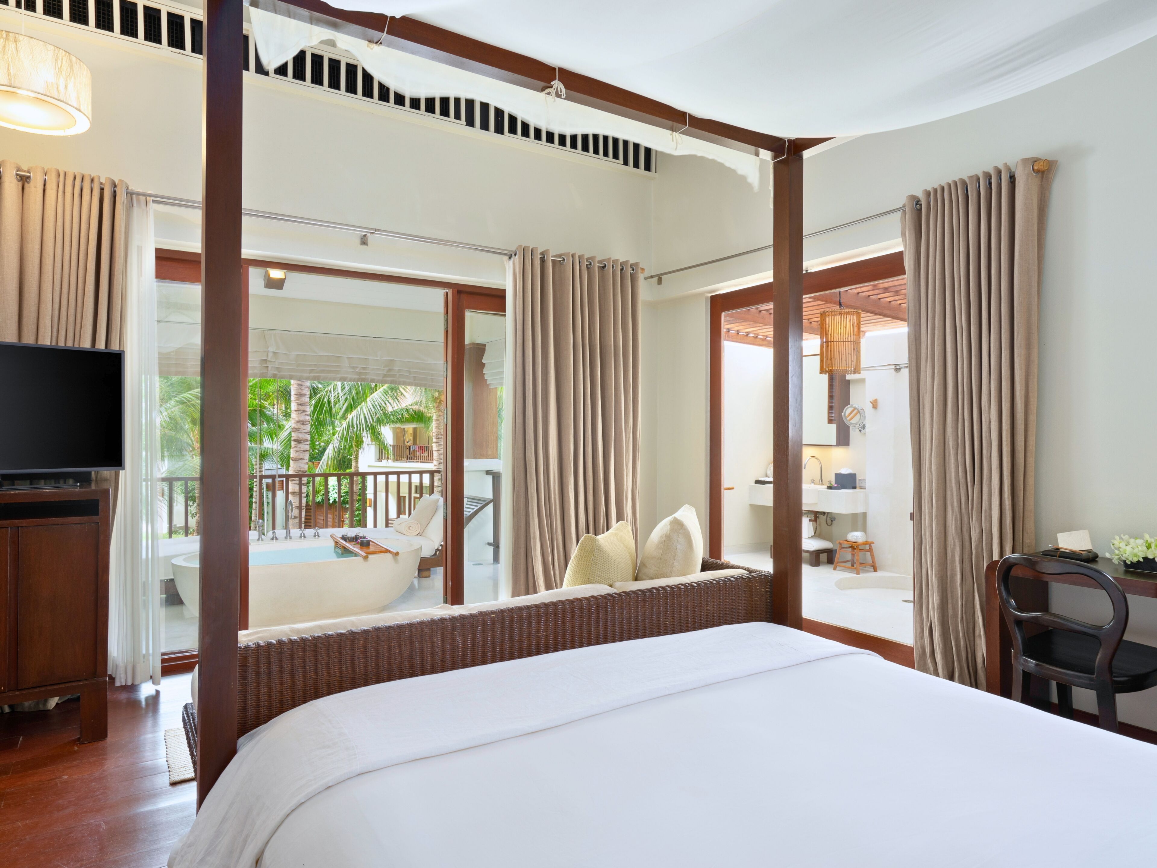 A hotel room with a large bed, a television, a balcony with a pool, and a view of palm trees.