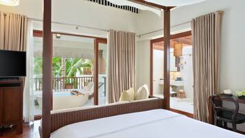 A hotel room with a large bed, a television, a balcony with a pool, and a view of palm trees.