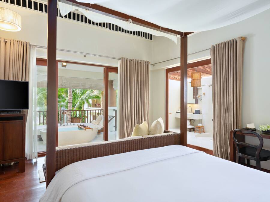 A hotel room with a large bed, a television, a balcony with a pool, and a view of palm trees.