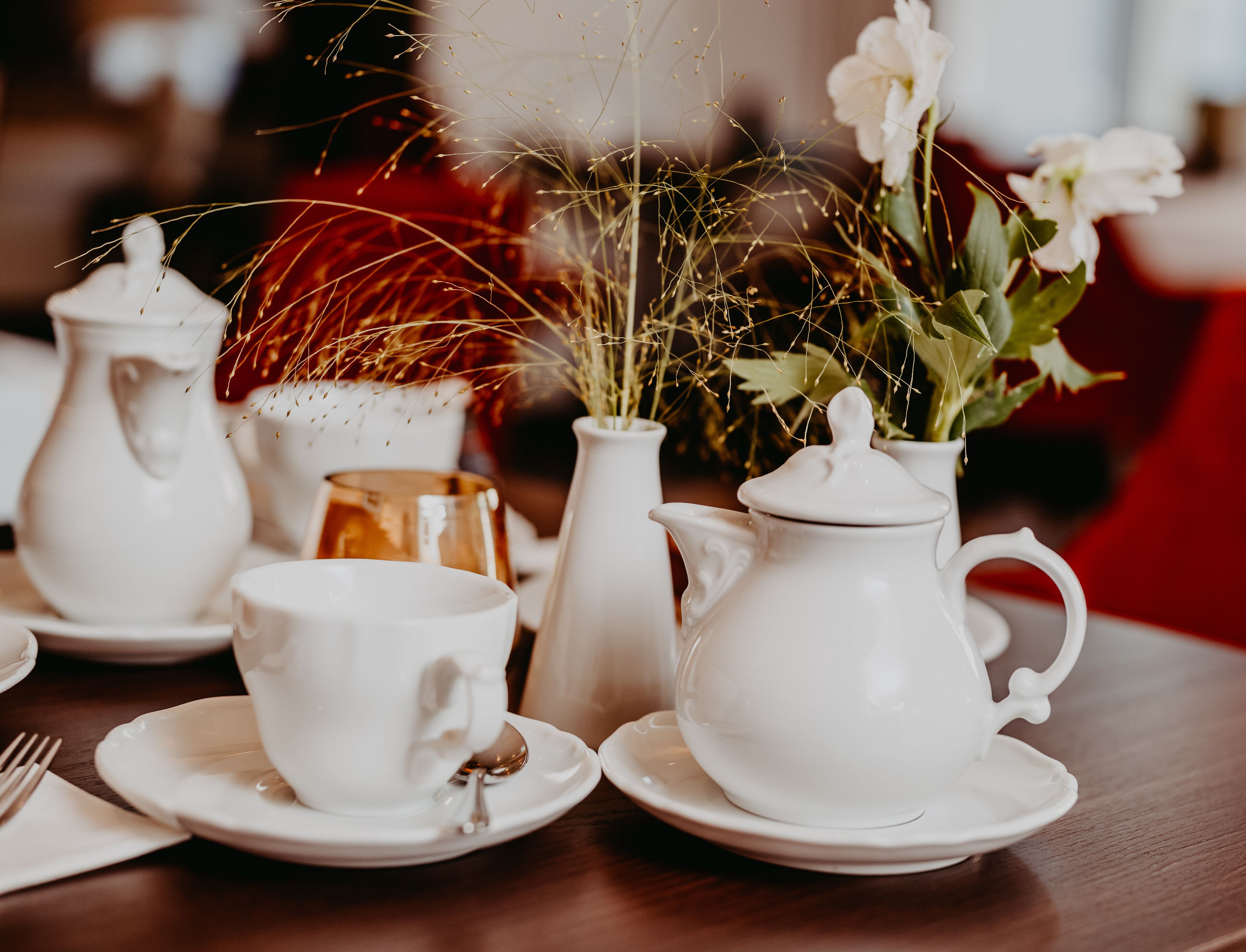 A table set with white teacups, saucers, a teapot, and a sugar bowl.