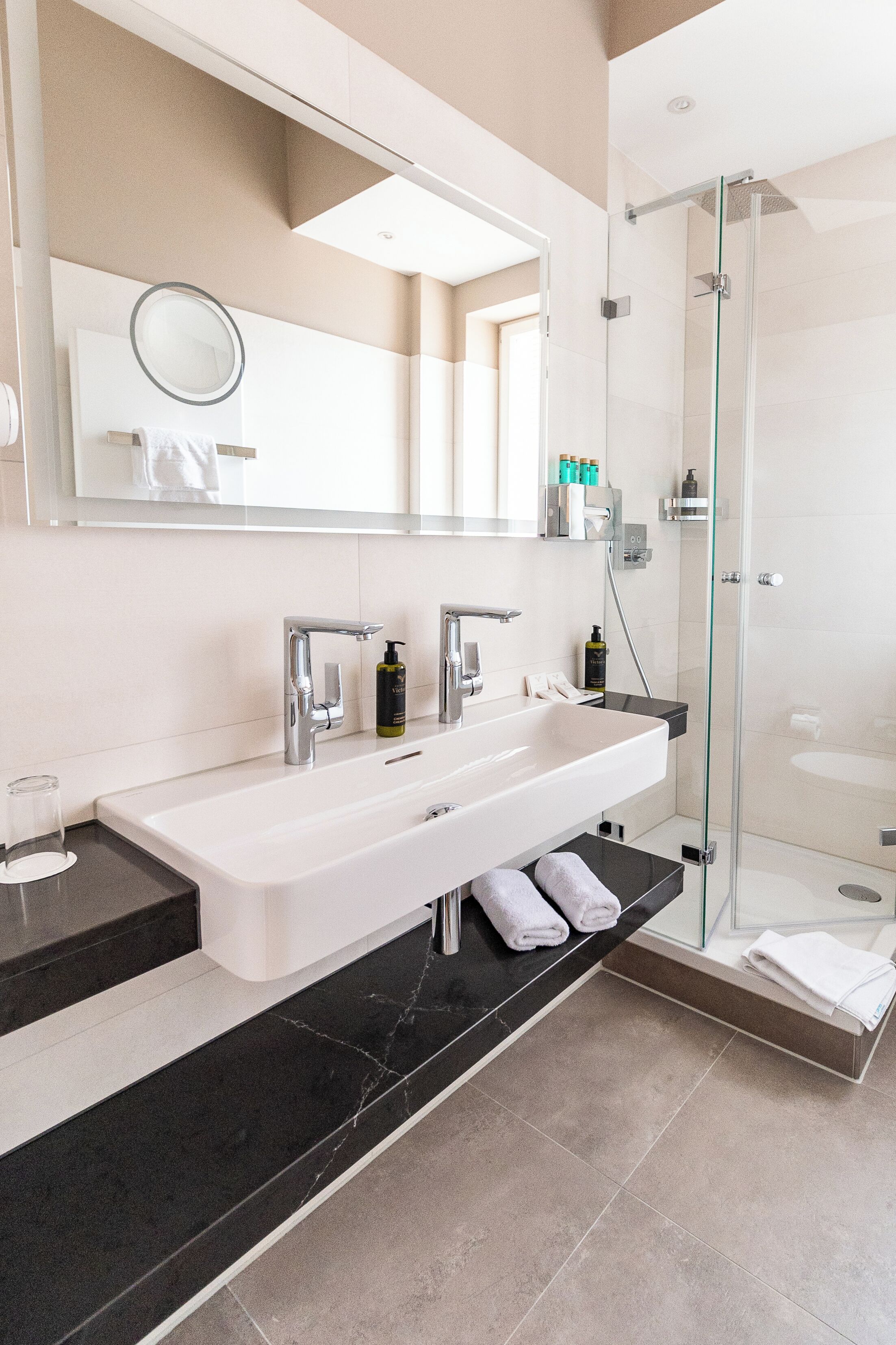 A modern bathroom with a large white sink, a glass-enclosed shower, and a mirror above the sink.