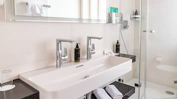 A modern bathroom with a large white sink, a glass-enclosed shower, and a mirror above the sink.