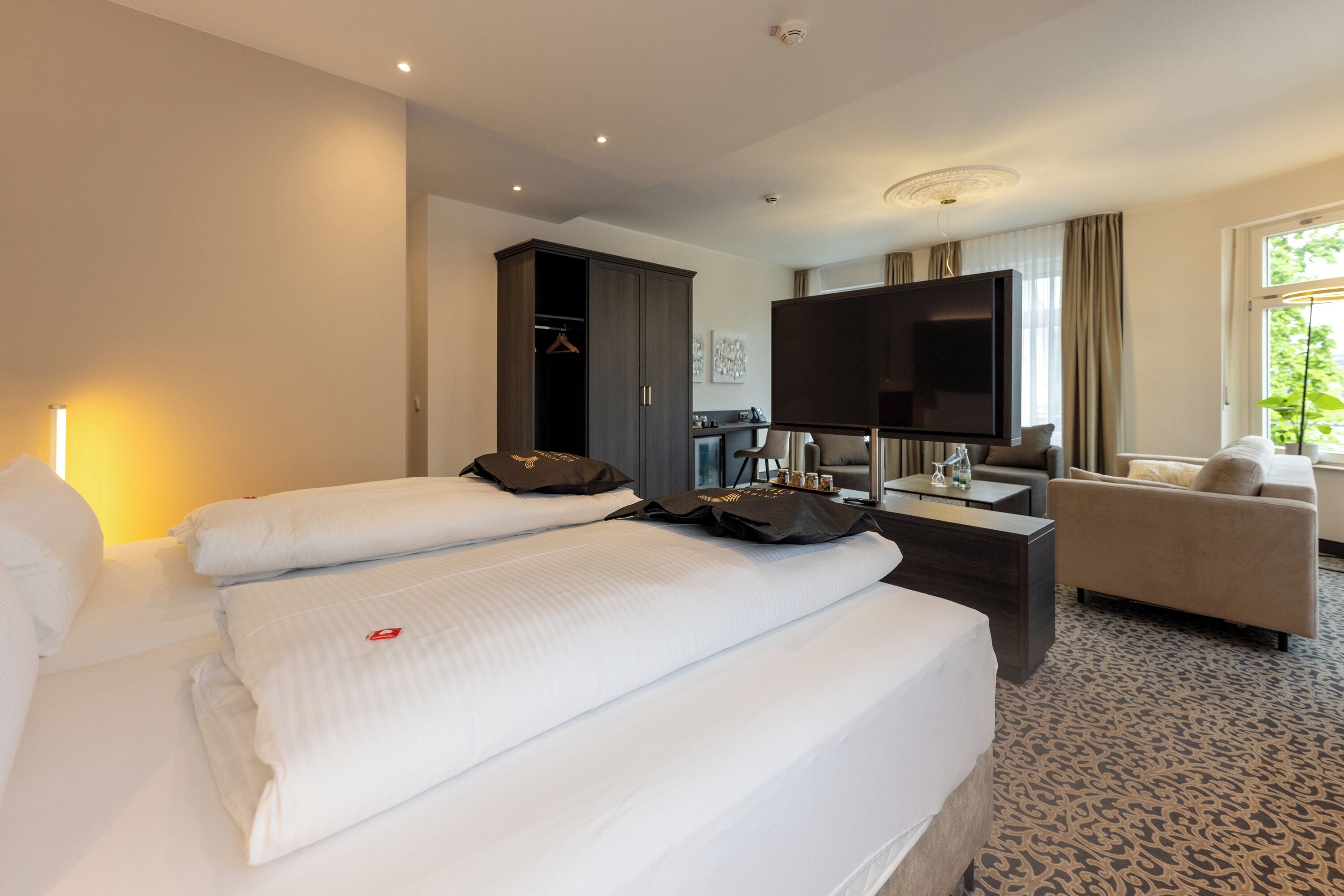 A hotel room with two beds, a TV, a desk, a sofa, and a wardrobe.