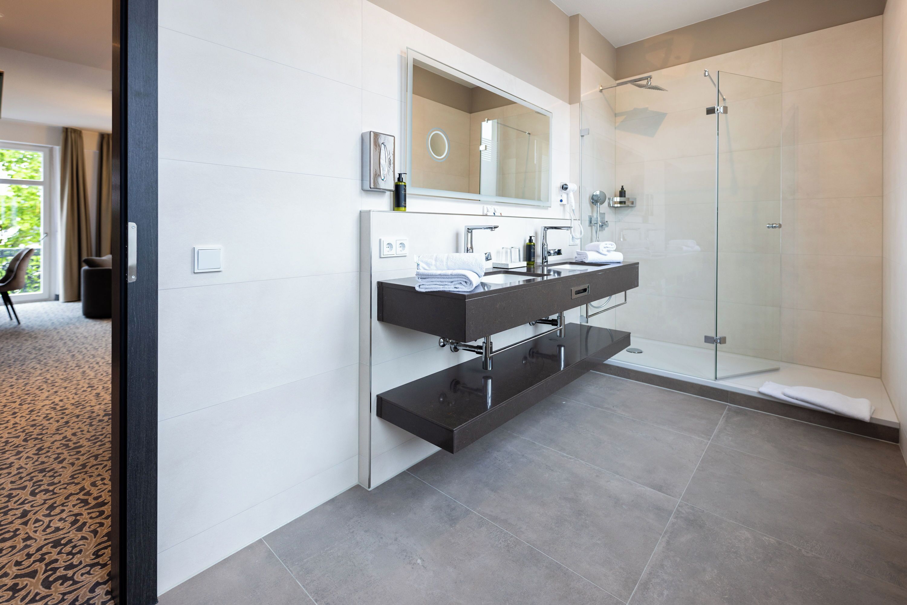Une salle de bain moderne dotée d’une douche à parois de verre, d’un meuble-lavabo à deux vasques et d’un grand miroir.