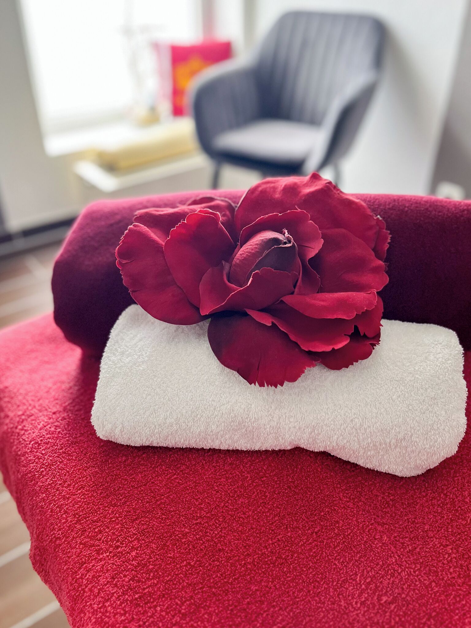 Ein roter, gepolsterter Sessel mit einem weißen Handtuch und einer großen roten Blütenblumen-Dekoration.
