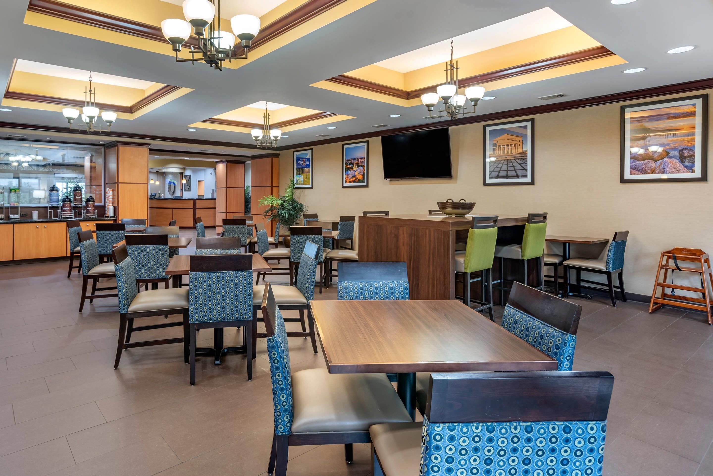 A spacious dining area with multiple tables and chairs, a central bar, and a television mounted on the wall.