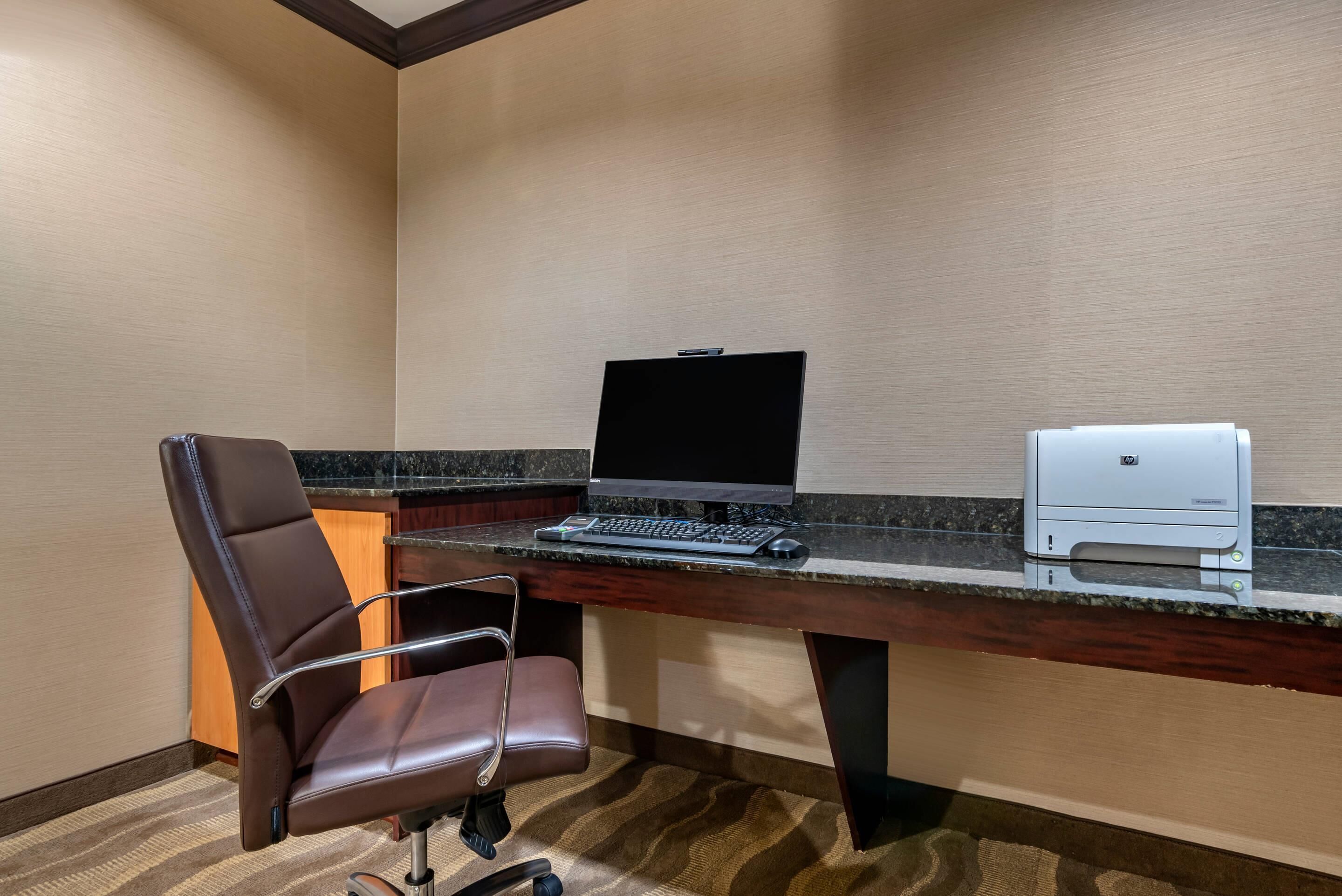 A hotel office with a desk, laptop, printer, and leather chair.