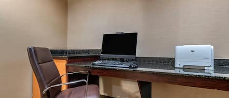 A hotel office with a desk, laptop, printer, and leather chair.