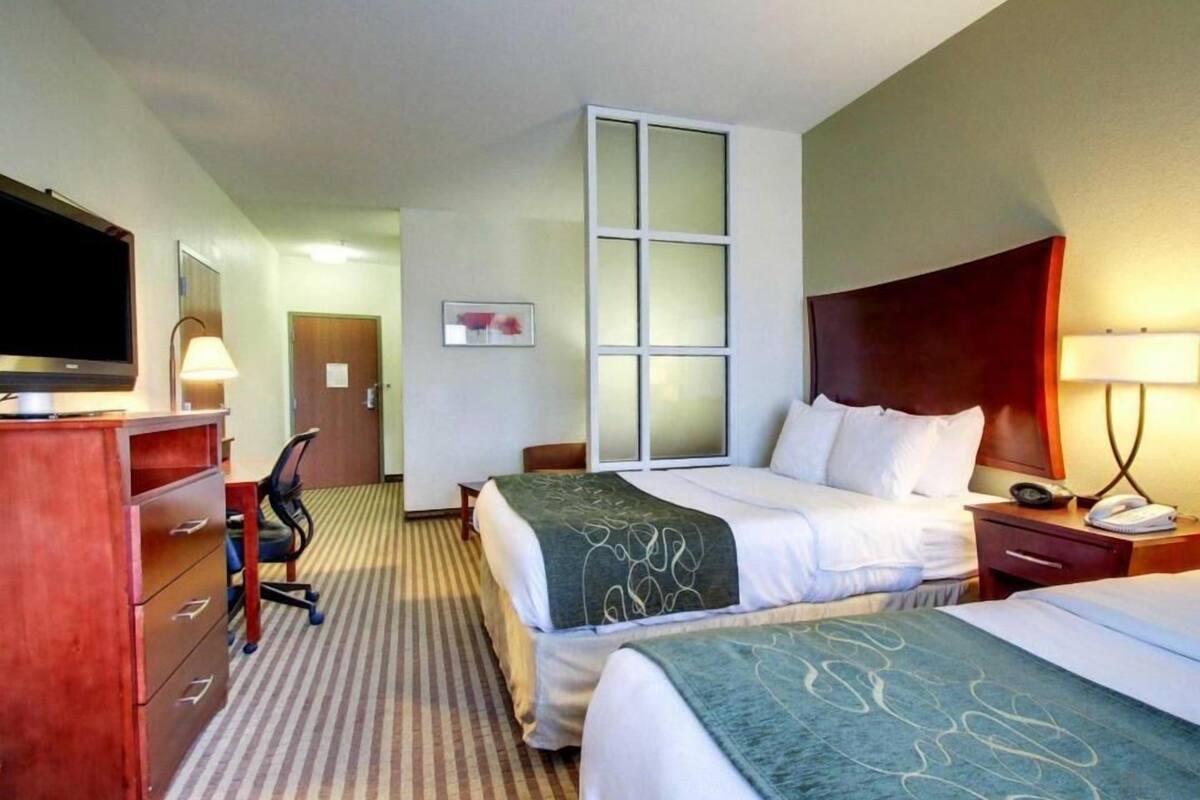A hotel room with two beds, a desk, a TV, and a window.