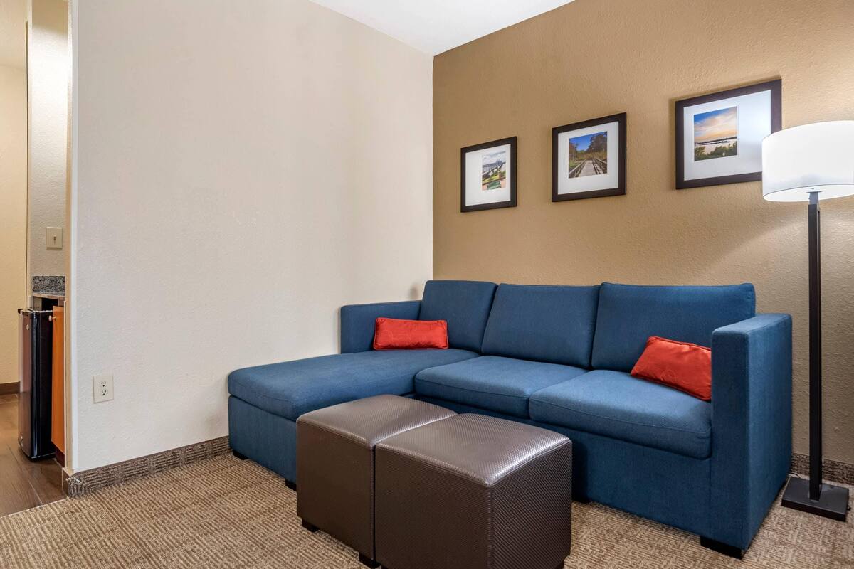 A room with a blue sectional sofa, a brown ottoman, and three framed pictures on the wall.