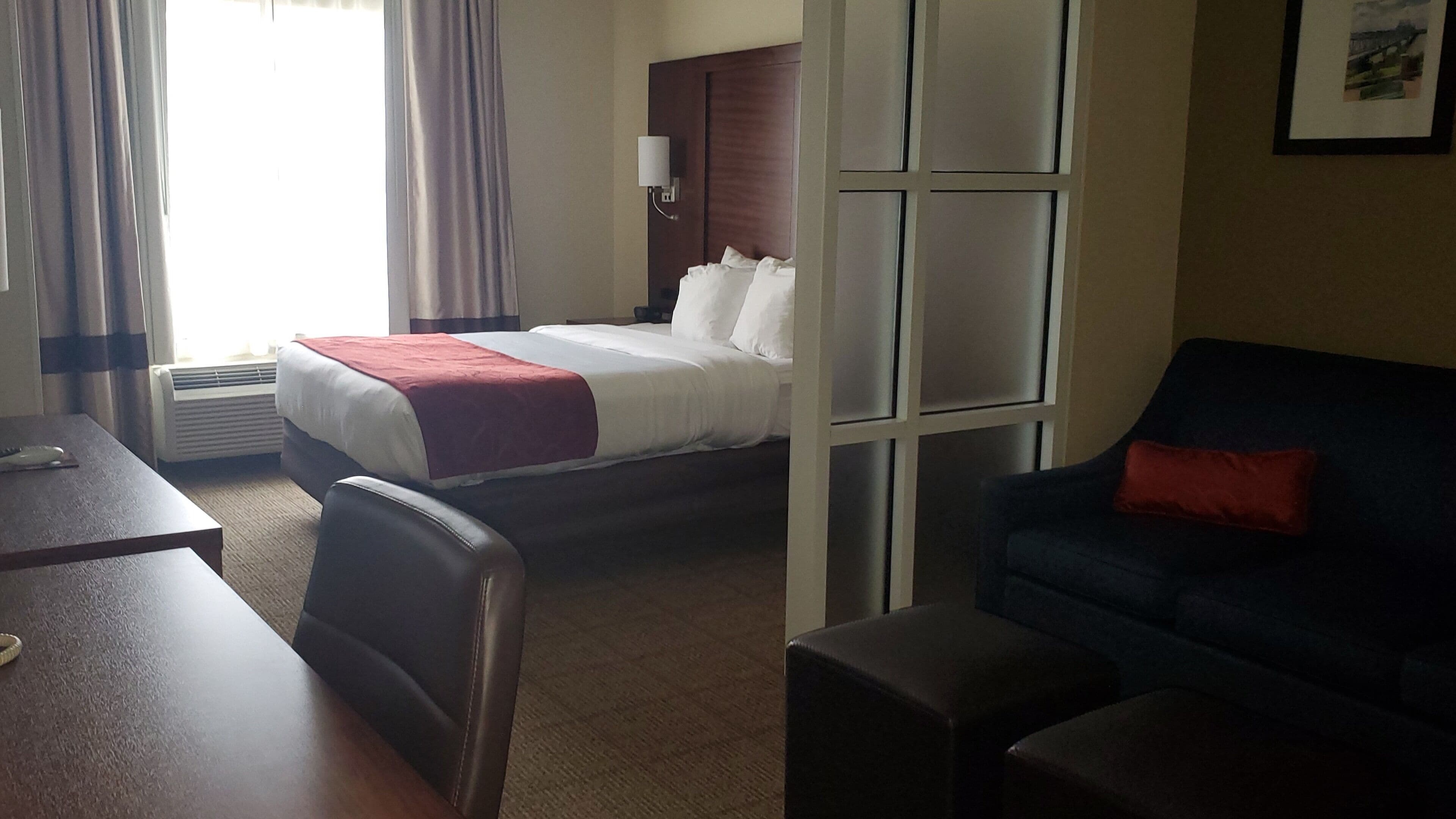A hotel room with a bed, a desk, a chair, a sofa, and a window.