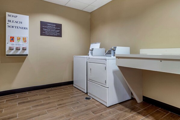 A laundry area with a sign for soap, bleach, and softeners, a guest laundry notice, and a washing machine.