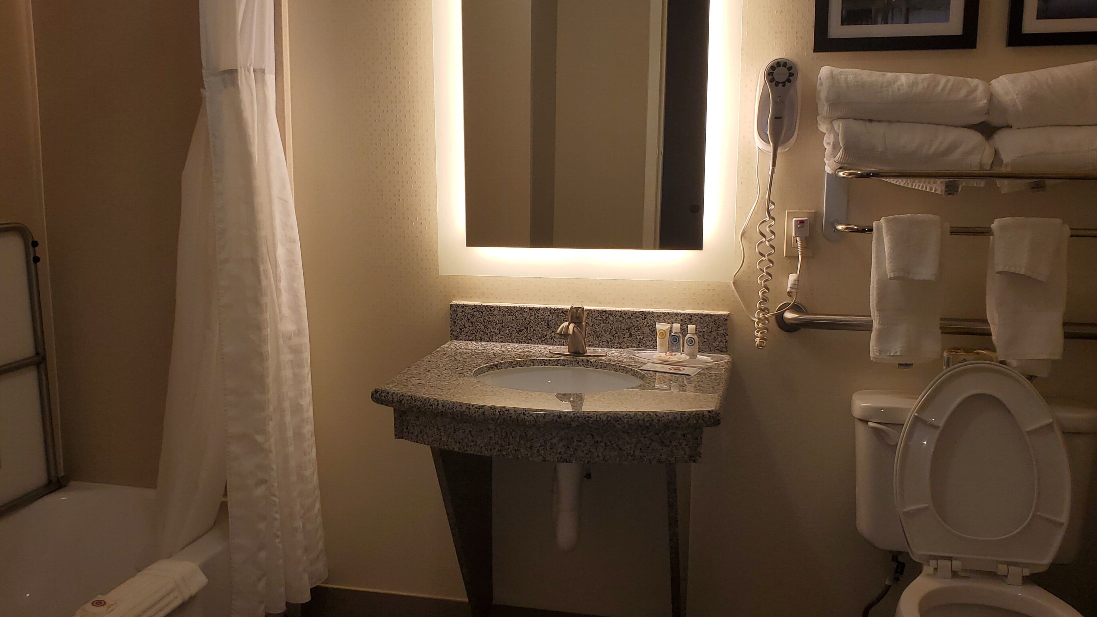 A bathroom with a granite sink, a toilet, a hairdryer, and a towel rack.