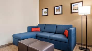 Un canapé d’angle bleu avec des coussins rouges, un pouf marron et une lampe sur pied.