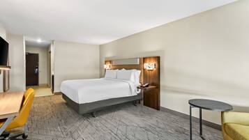 A hotel room with a bed, bedside table, chair, desk, and a small round table.