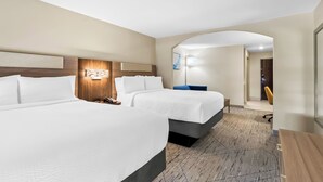 Una habitación de hotel con dos camas, cabecero de madera, un escritorio y una silla.