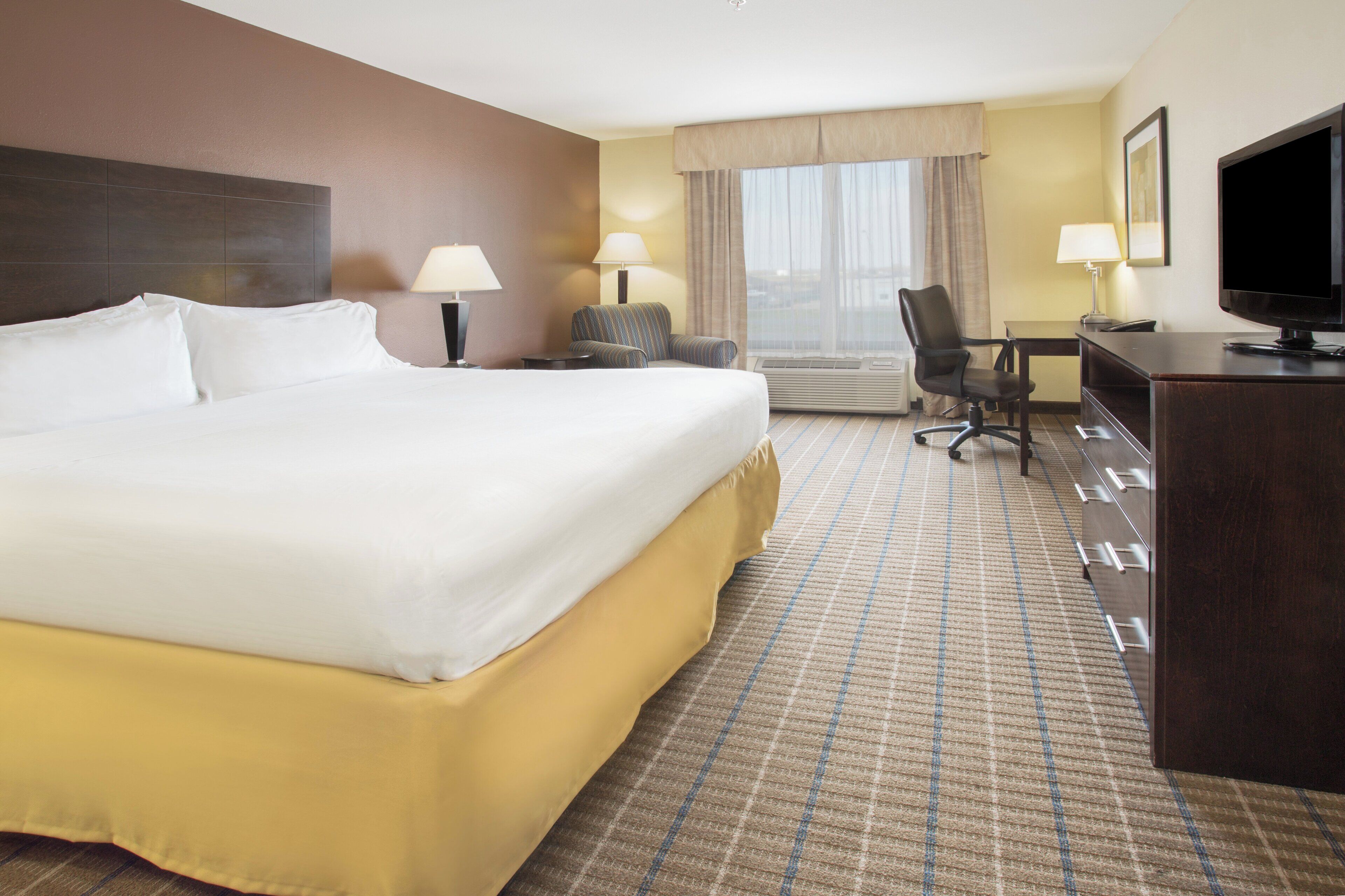 A hotel room with a large bed, a desk, a chair, and a television.
