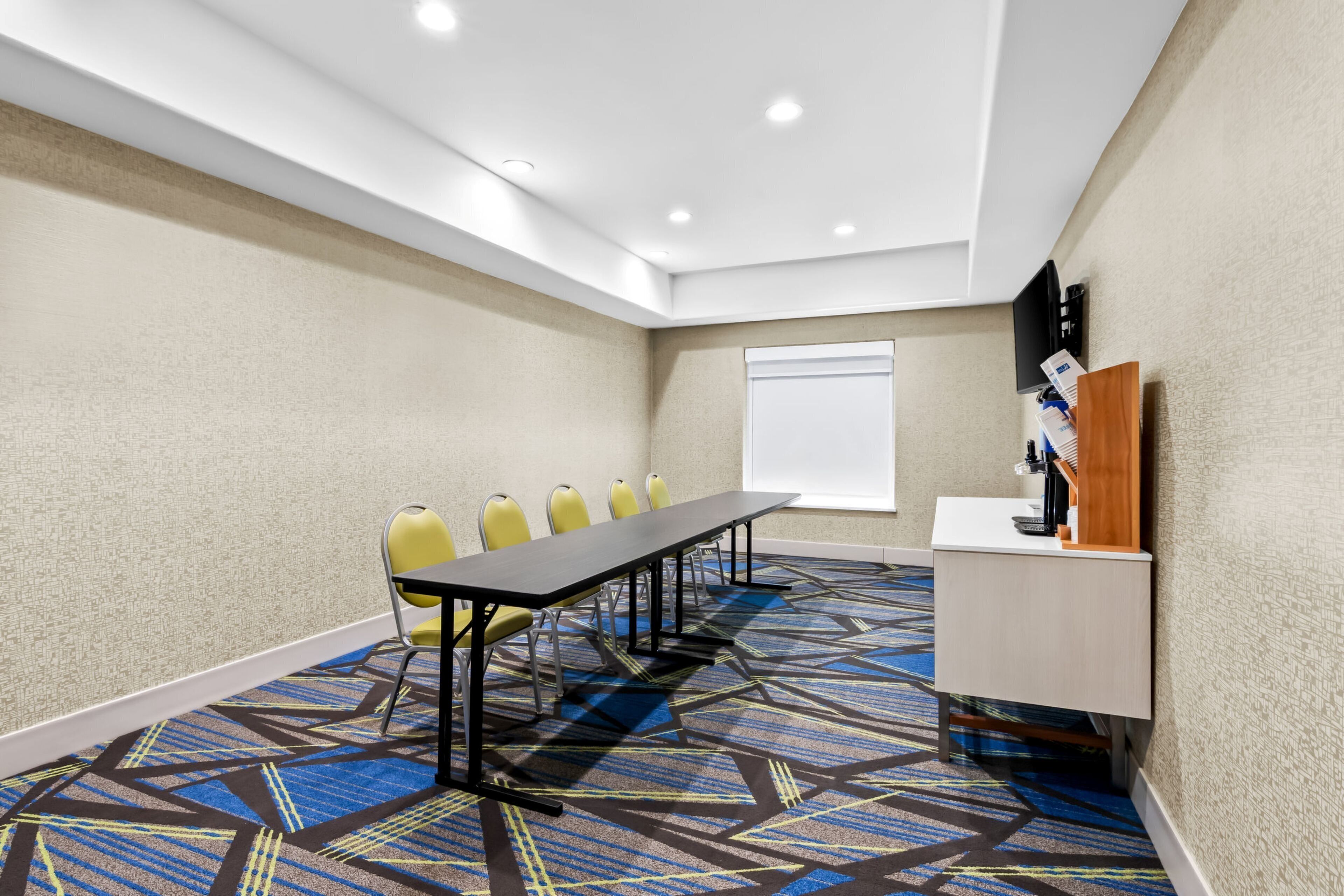 Una sala conferenze con un lungo tavolo, sedie gialle, una lavagna e una scrivania con un computer.