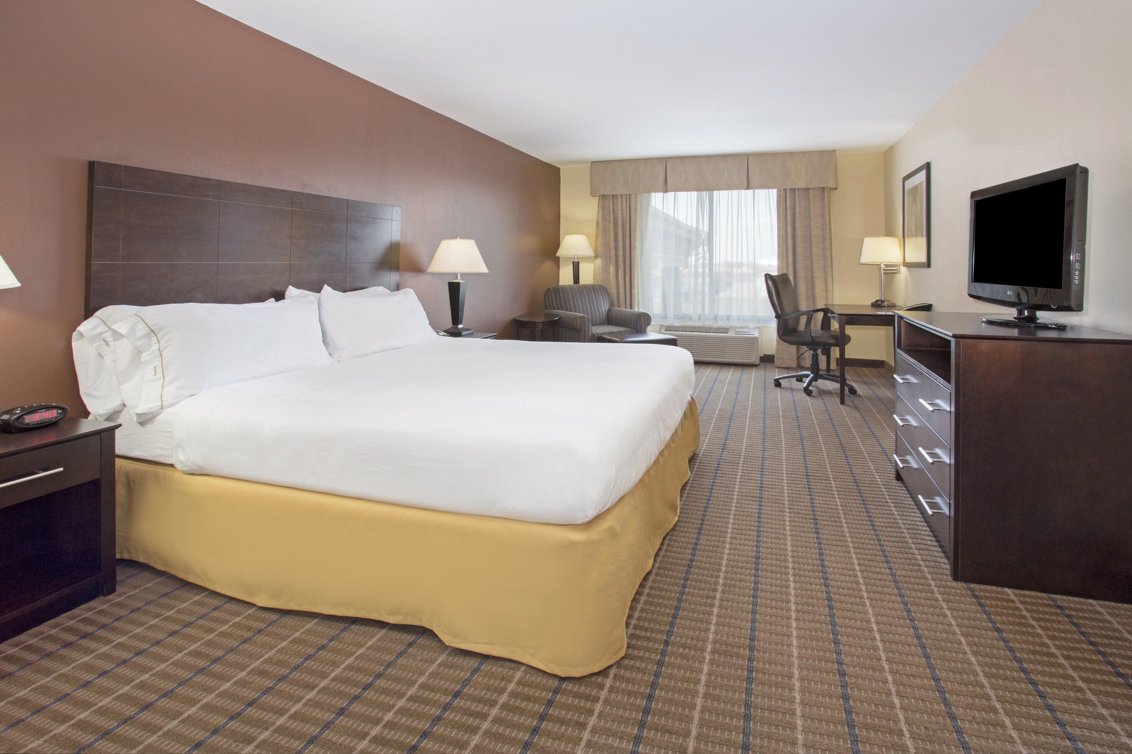 A hotel room with a large bed, a desk, a chair, a television, and a window with curtains.