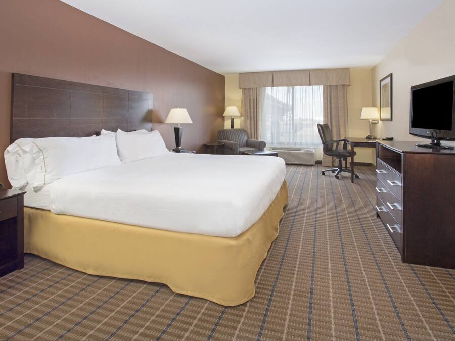 A hotel room with a large bed, a desk, a chair, a television, and a window with curtains.
